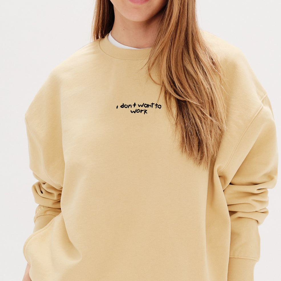 Woman wearing a yellow sweatshirt with an I don't want to work embroidered text