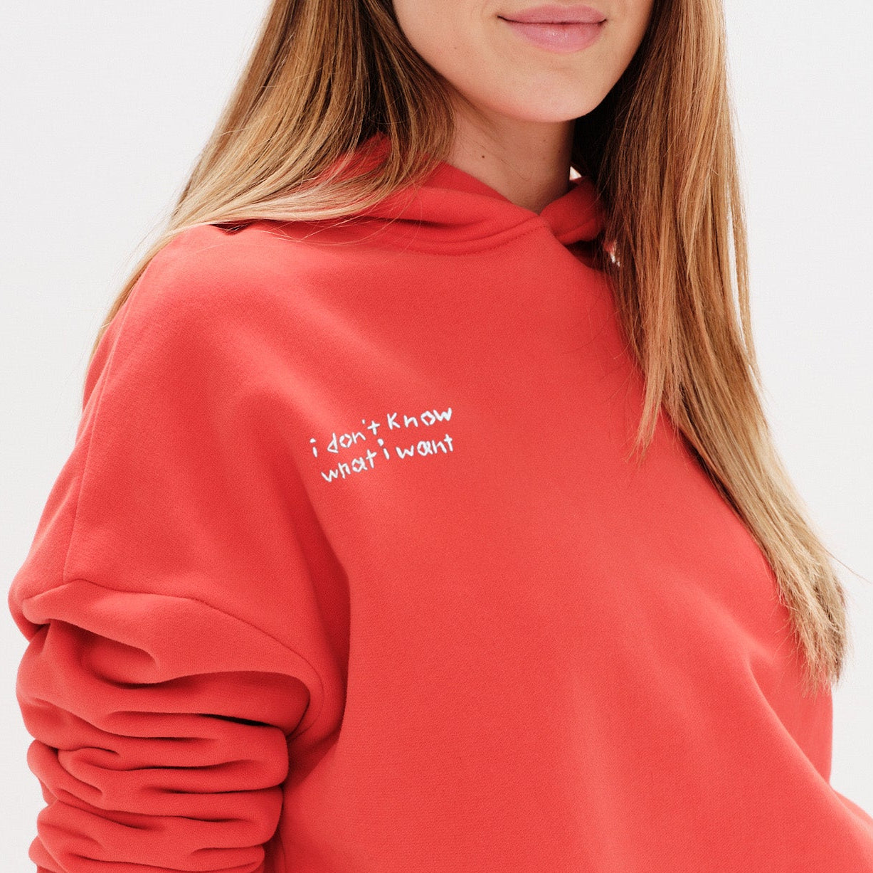 Woman wearing an orange hoodie with an I don't know what I want embroidery text