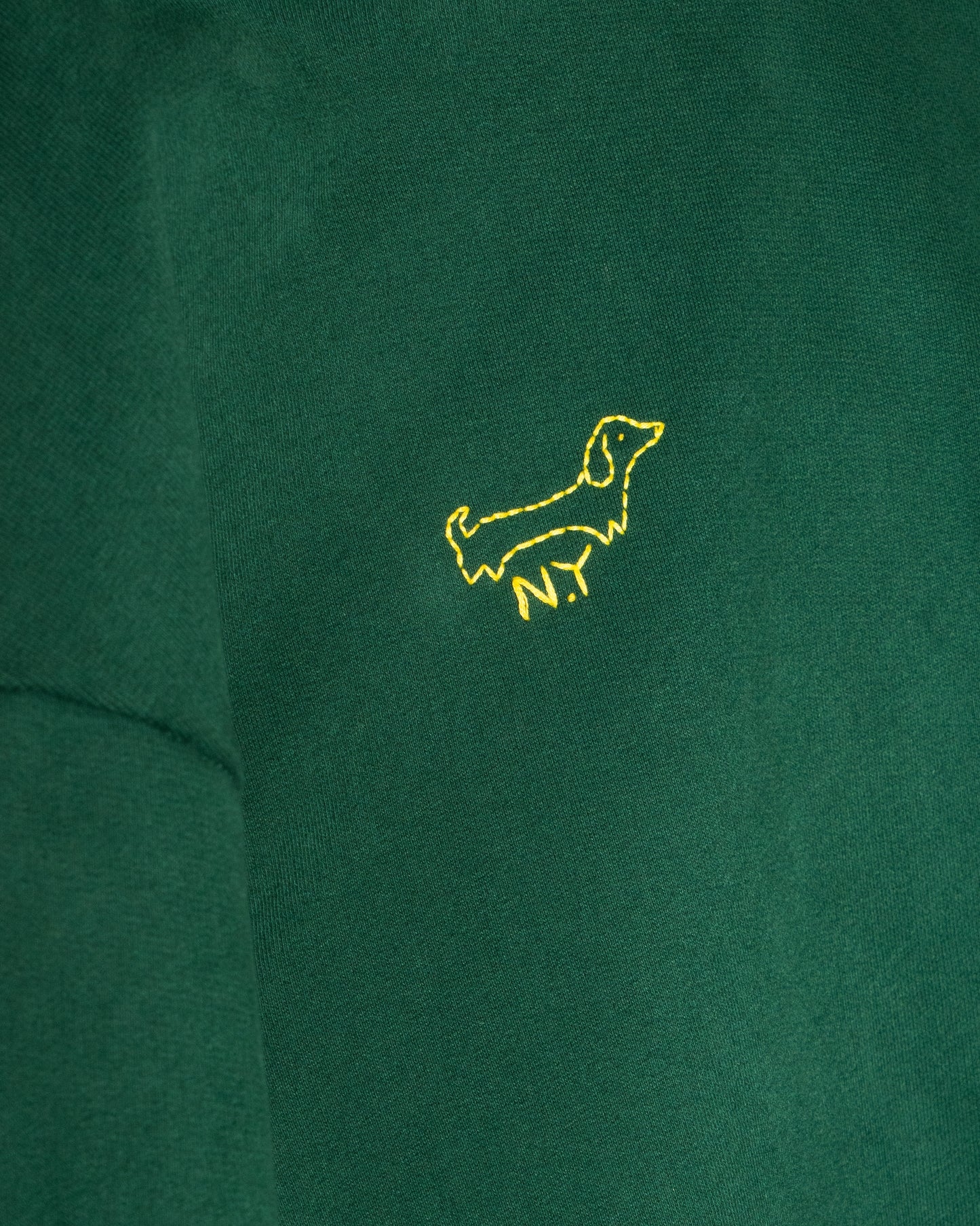 Close-up of a green hoodie featuring a small, yellow embroidered embellishment in the shape of a dog.