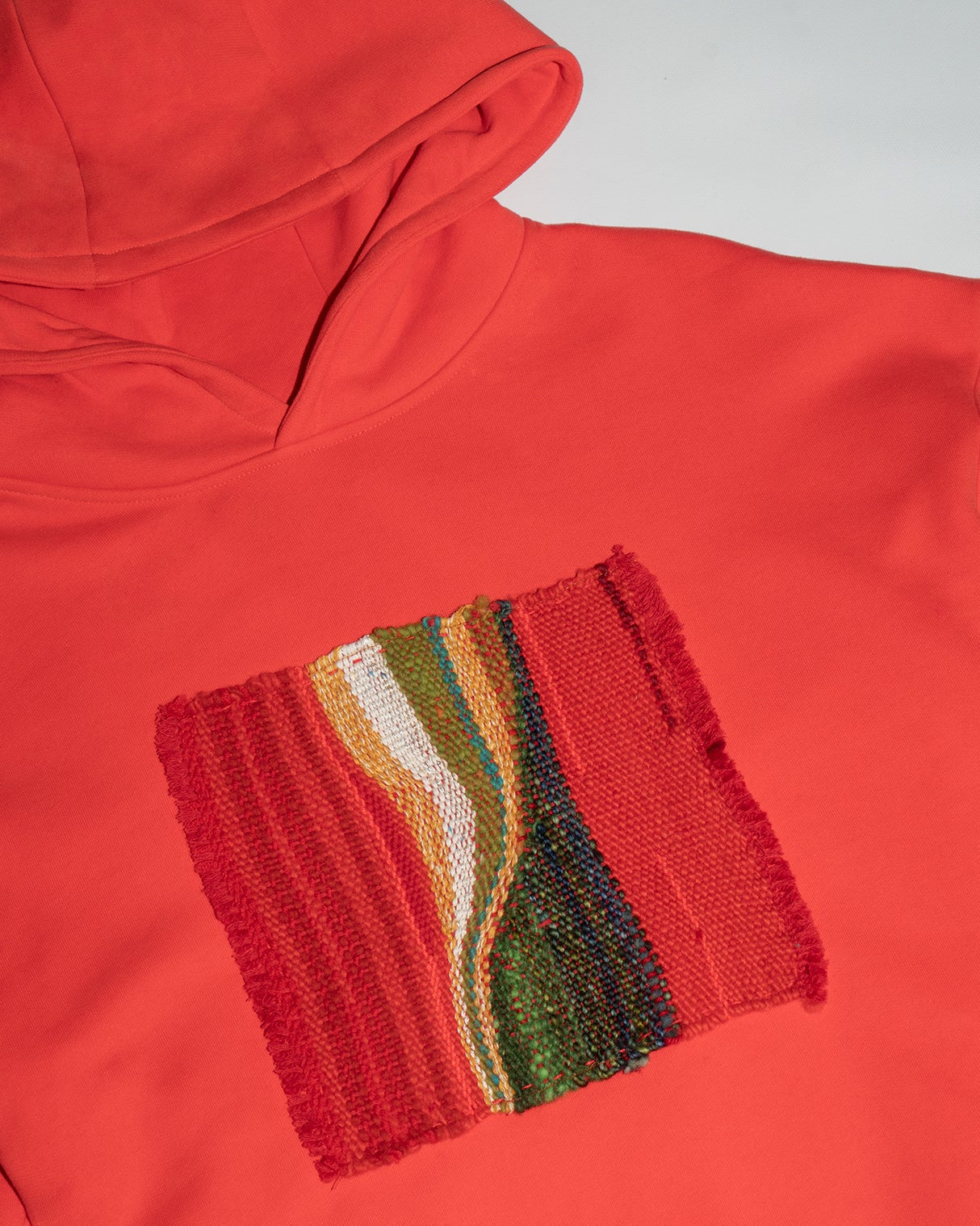 Red hoodie with a colorful knitted pocket on a light gray background