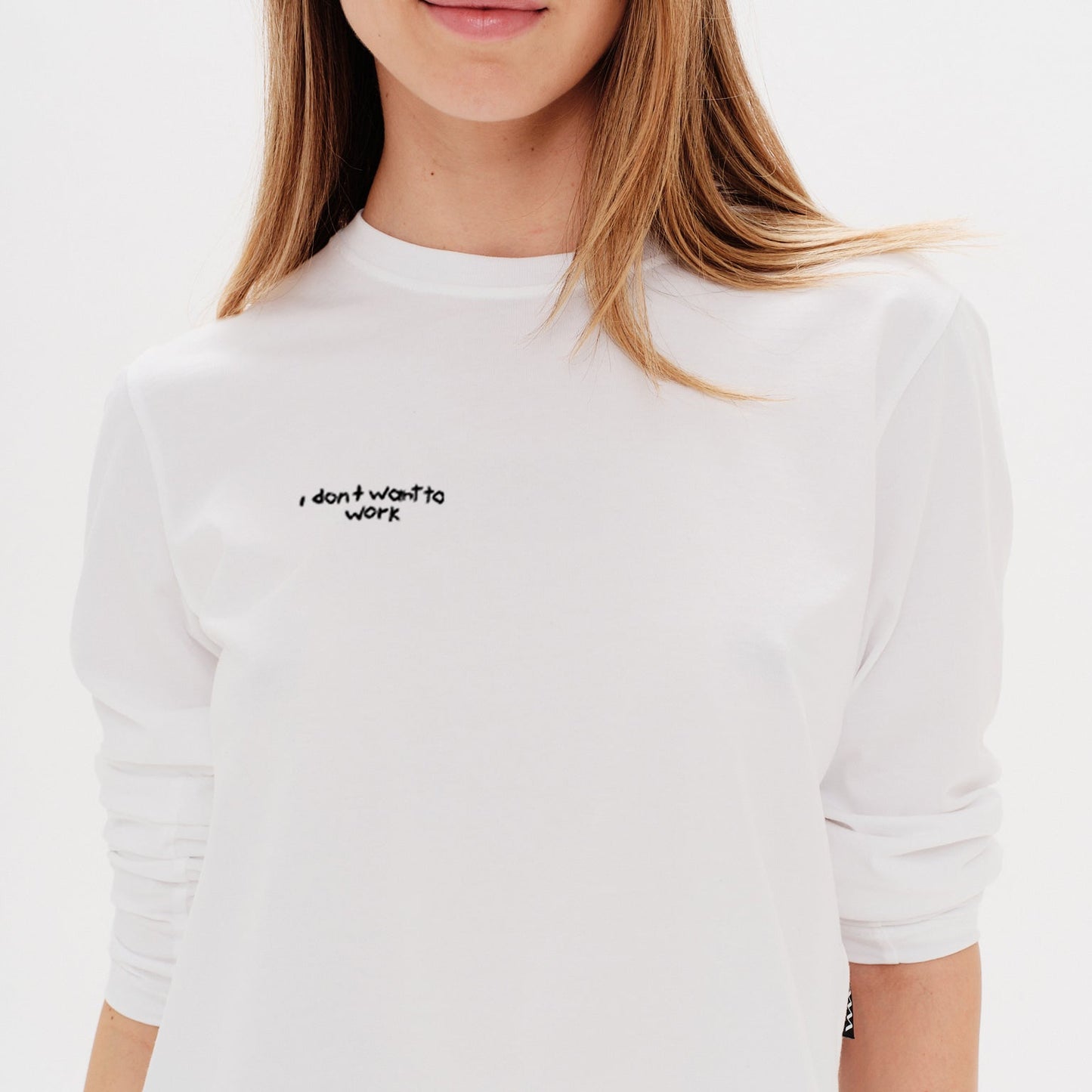 Woman wearing a white long-sleeve crop top with an I don't want to work embroidery