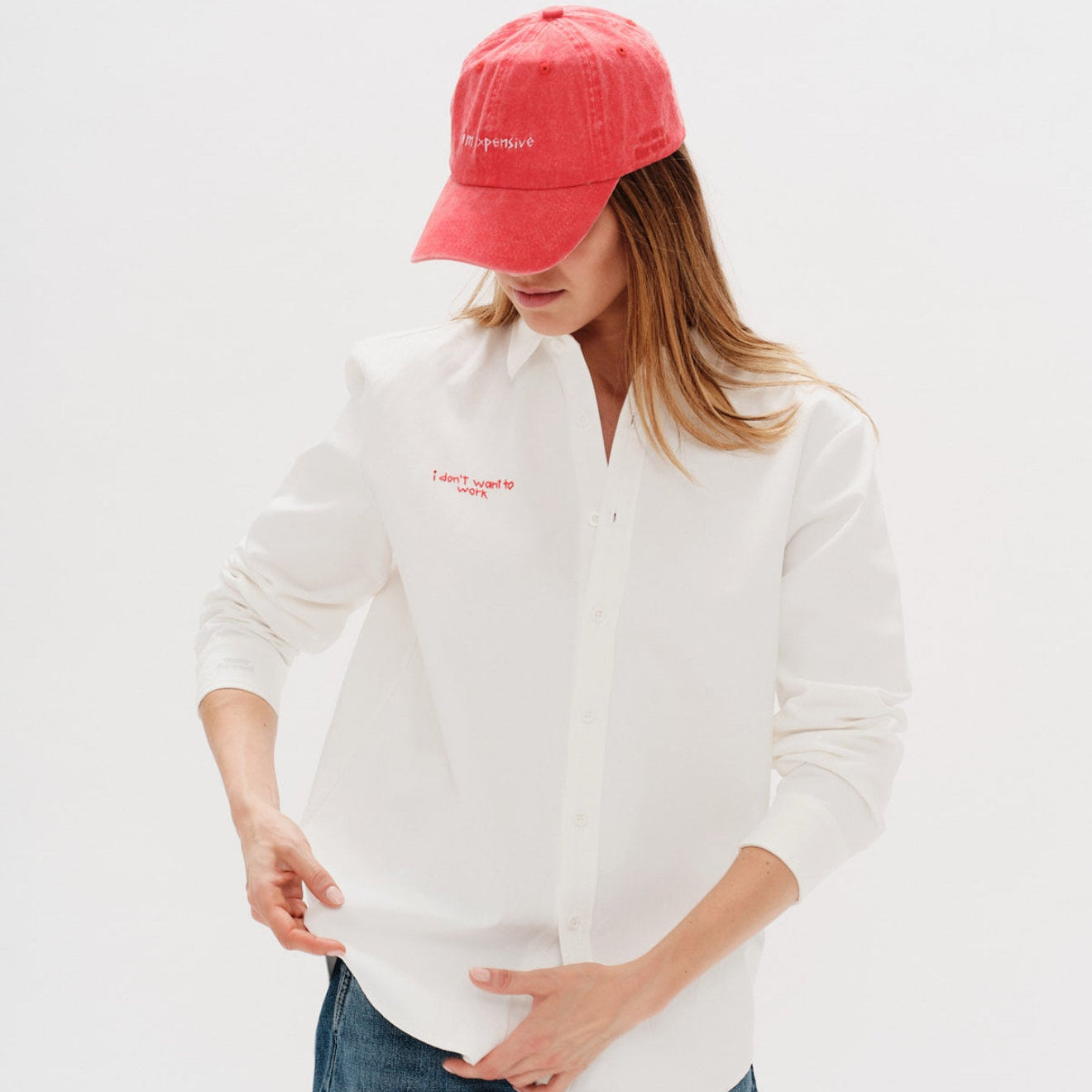 Woman wearing a white shirt, blue jeans, and a red cap on a light gray background