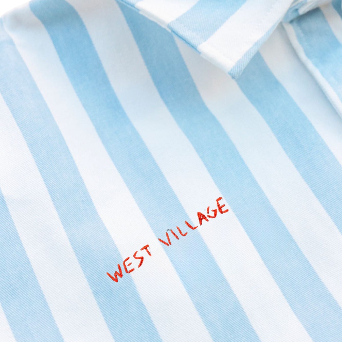 Close-up of a blue and white striped shirt with 'West Village' embroidery.