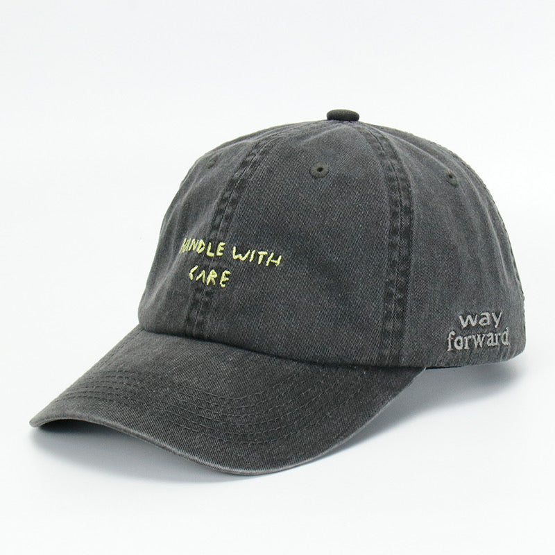 A black cotton cap with the phrase 'HANDLE WITH CARE' embroidered on the front.
