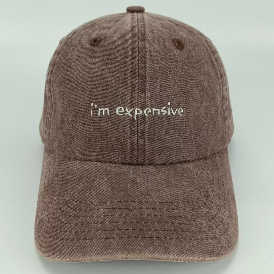 A brown wash baseball cap with the phrase 'I am expensive' embroidered on the front.