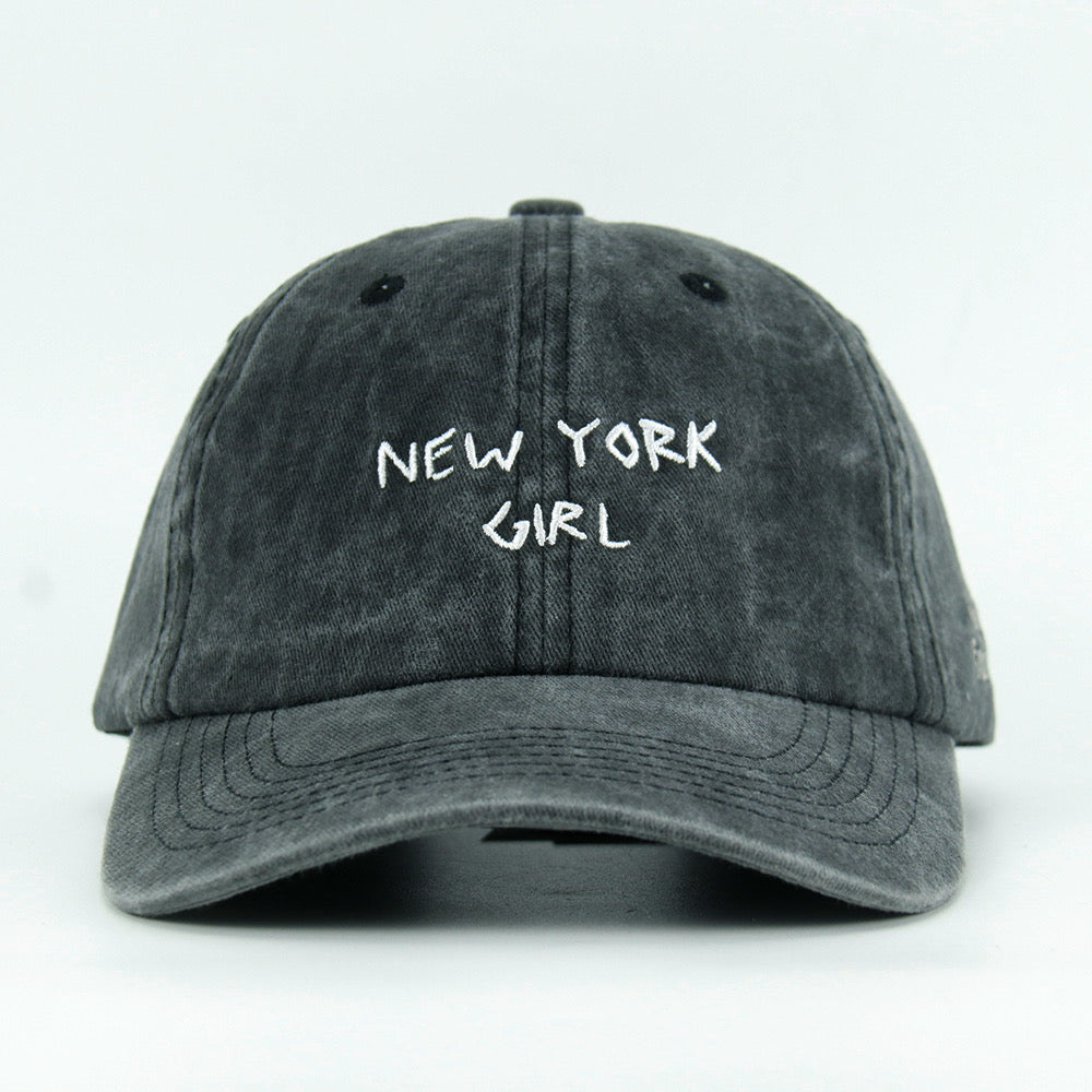 A washed black baseball cap with 'NEW YORK GIRL' embroidered in white on the front.