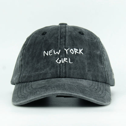 A washed black baseball cap with 'NEW YORK GIRL' embroidered in white on the front.