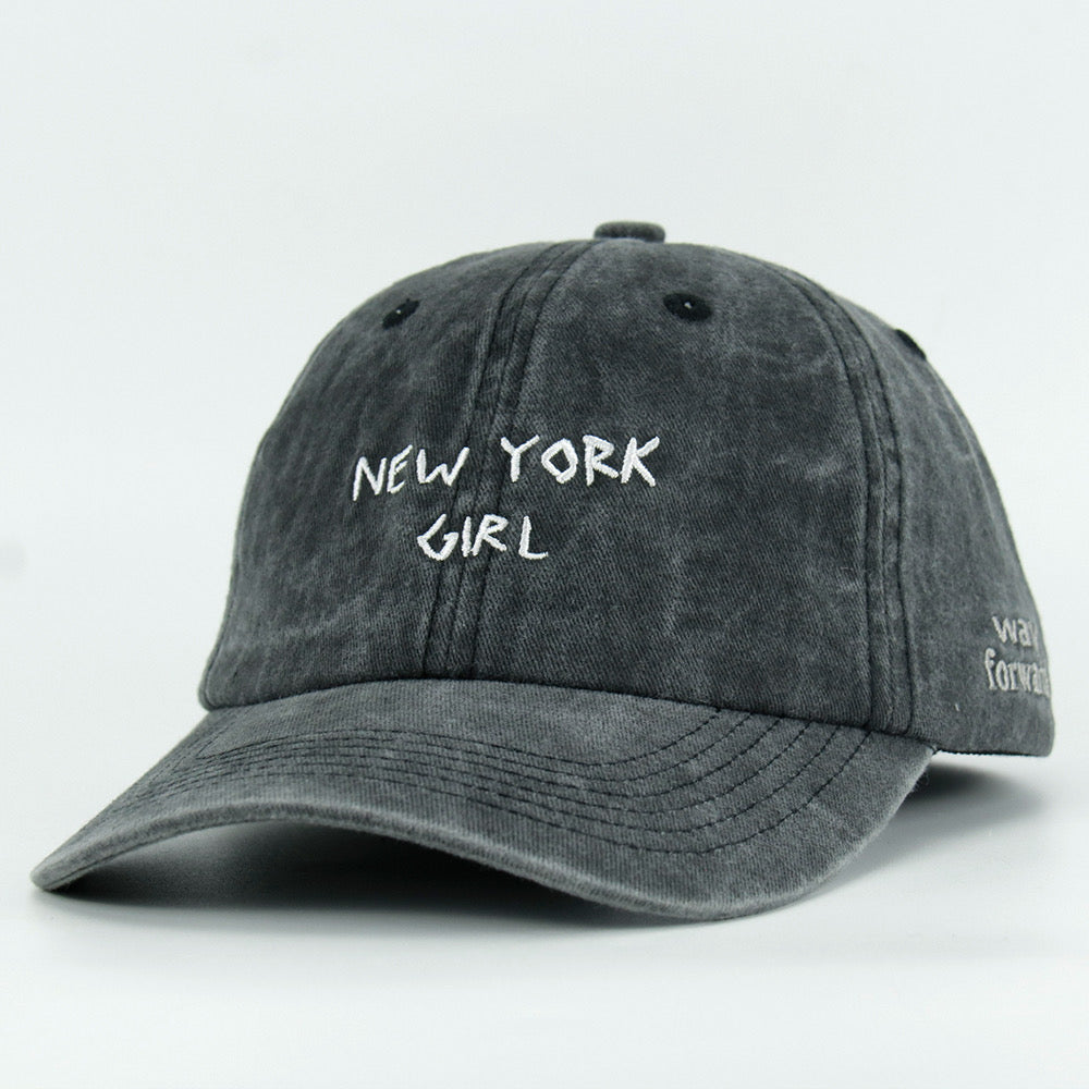 A washed black baseball cap with 'NEW YORK GIRL' embroidered in white on the front.