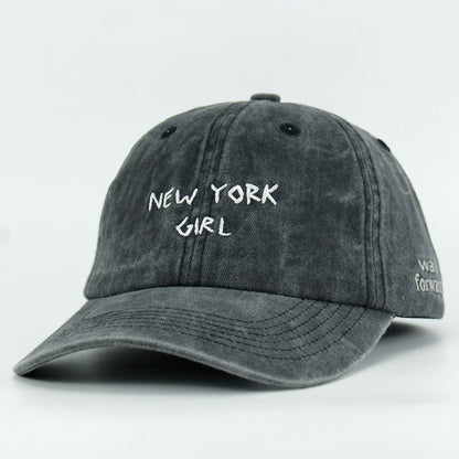 A washed black baseball cap with 'NEW YORK GIRL' embroidered in white on the front.