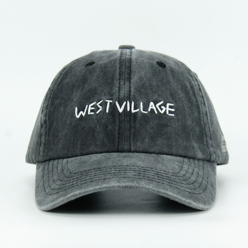 A washed black baseball cap with 'WEST VILLAGE' embroidered in white on the front.