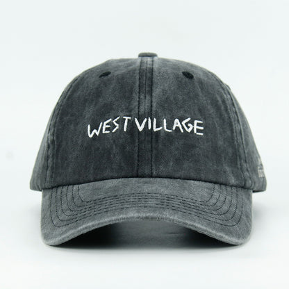 A washed black baseball cap with 'WEST VILLAGE' embroidered in white on the front.