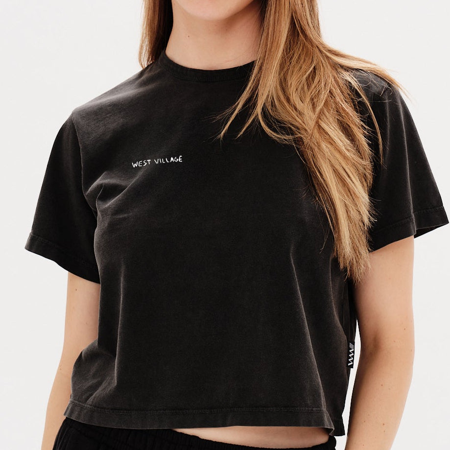 Woman wearing a black t-shirt with a West Village embrodery