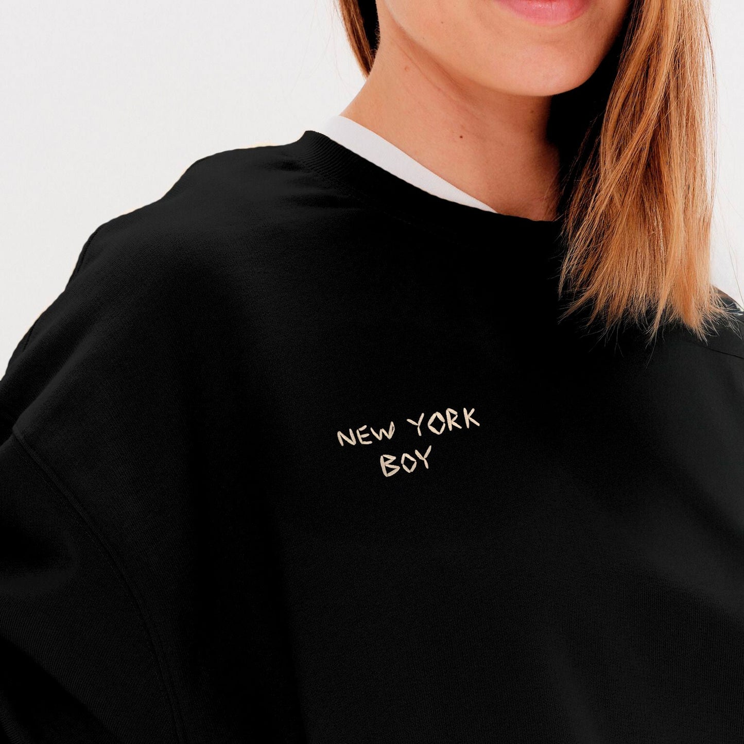 Woman wearing a black sweatshirt with New York Boy embroidered text