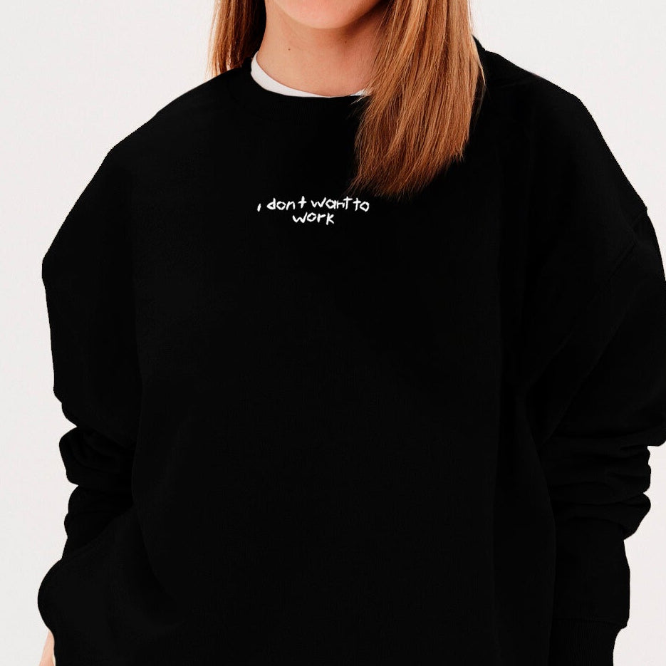 Woman wearing a black sweatshirt with an I don't want to work embroidered text