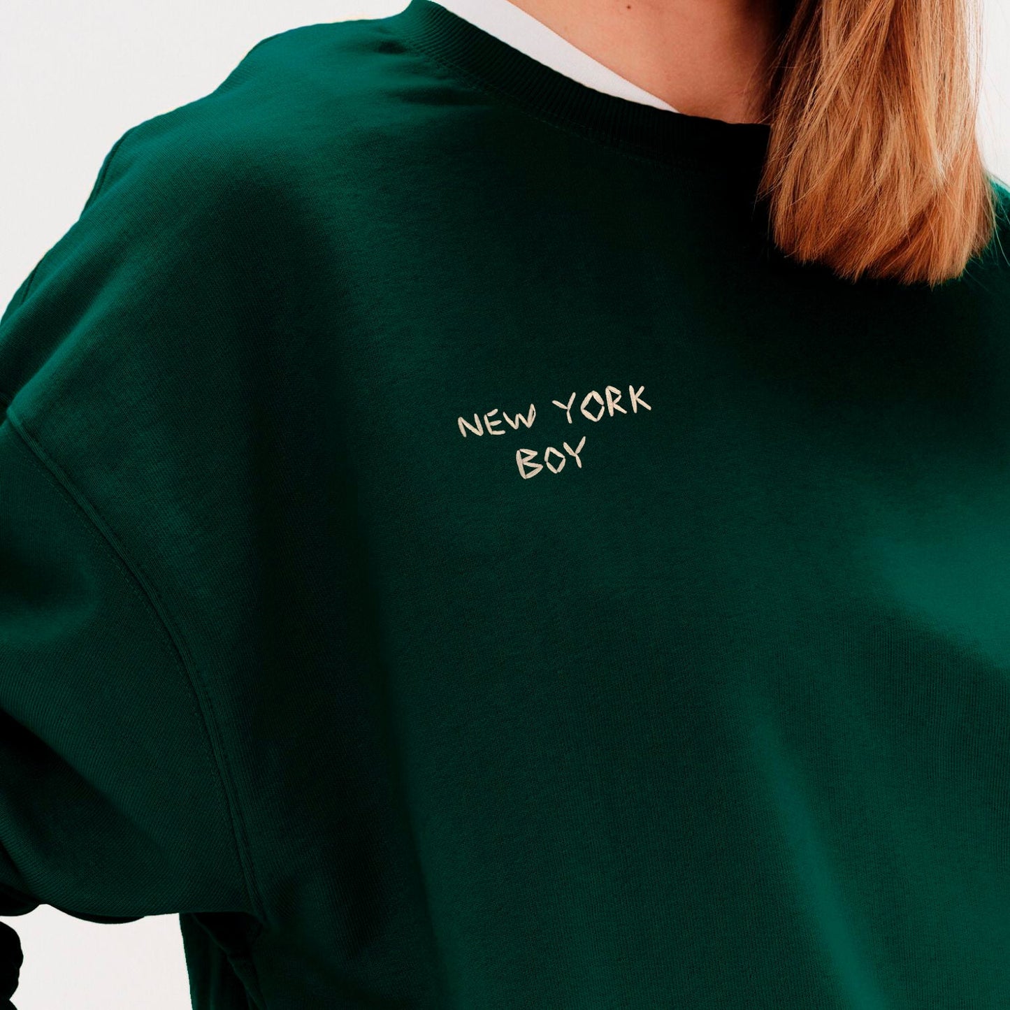 Woman wearing a green sweatshirt with New York Boy embroidered text