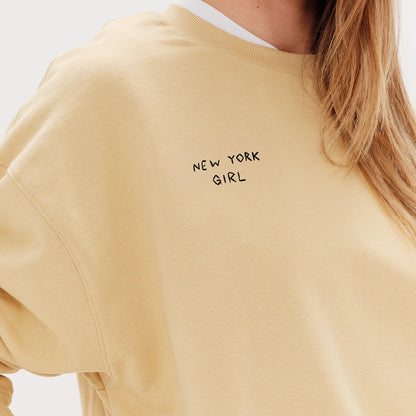 Woman wearing a yellow sweatshirt with a New York Girl embroidered text