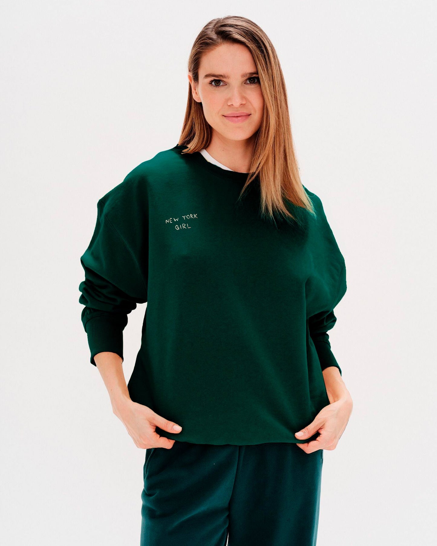 Woman wearing a green sweatshirt with a New York Girl embroidered text