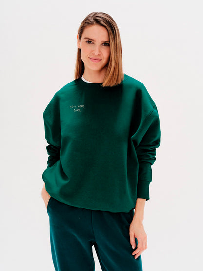 Woman wearing a green sweatshirt with a New York Girl embroidered text