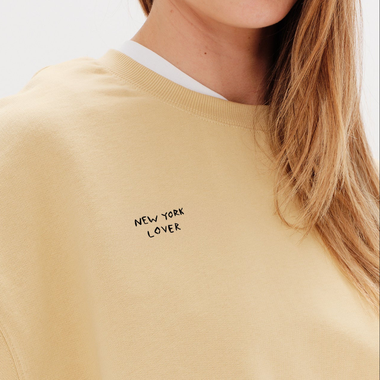 Woman wearing a yellow sweatshirt with New York Lover embroidered text