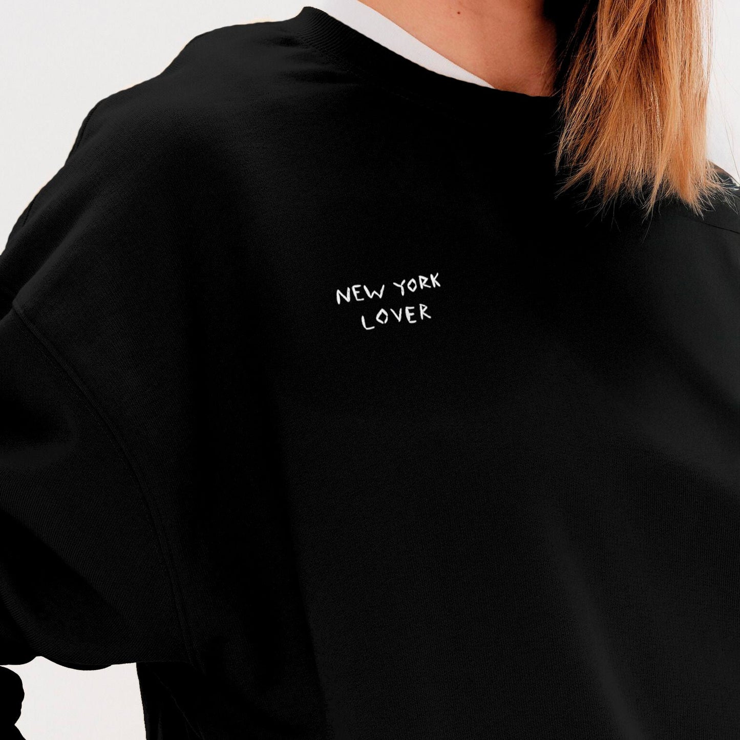 Woman wearing a black sweatshirt with an New York Lover embroidered text