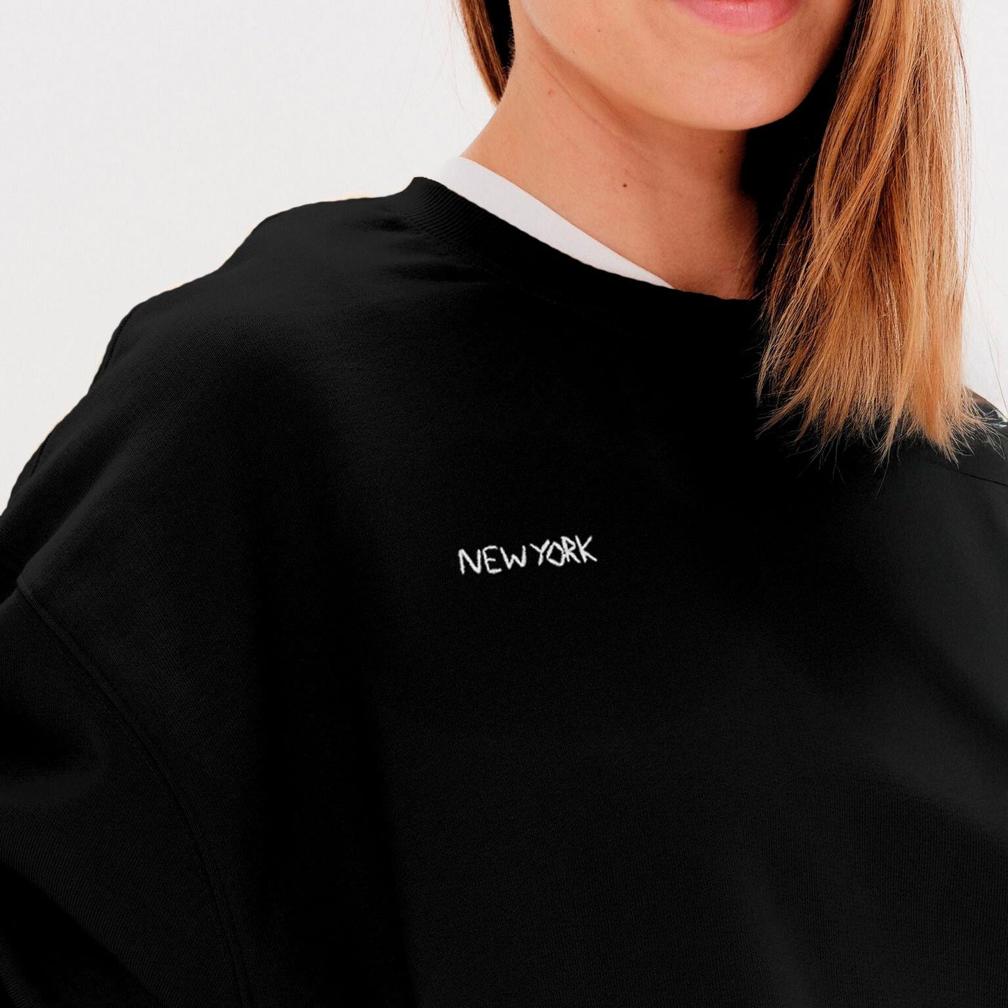 Woman wearing a black sweatshirt with 'New York' embroidery
