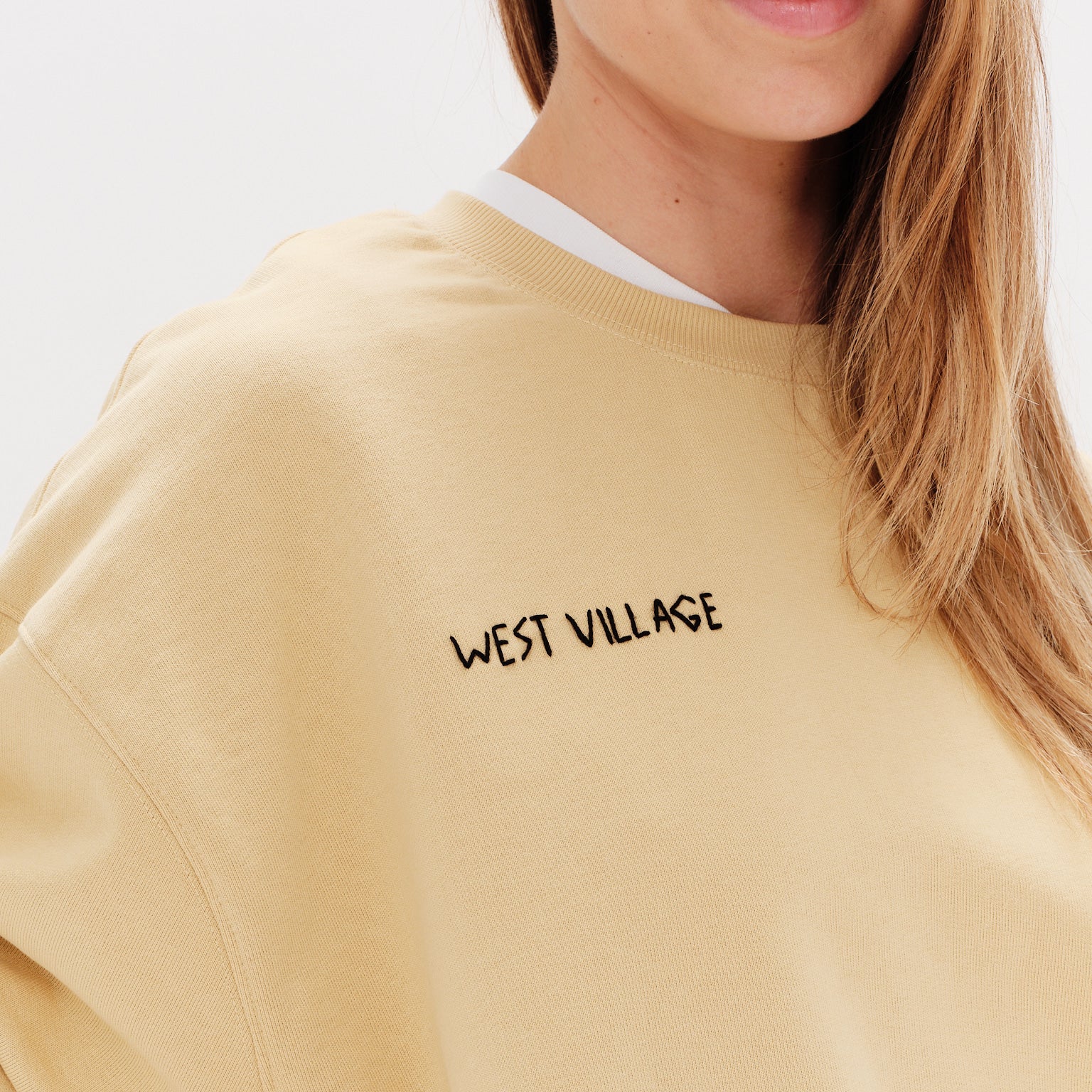 Woman wearing a yellos sweatshirt with embroidered west village text