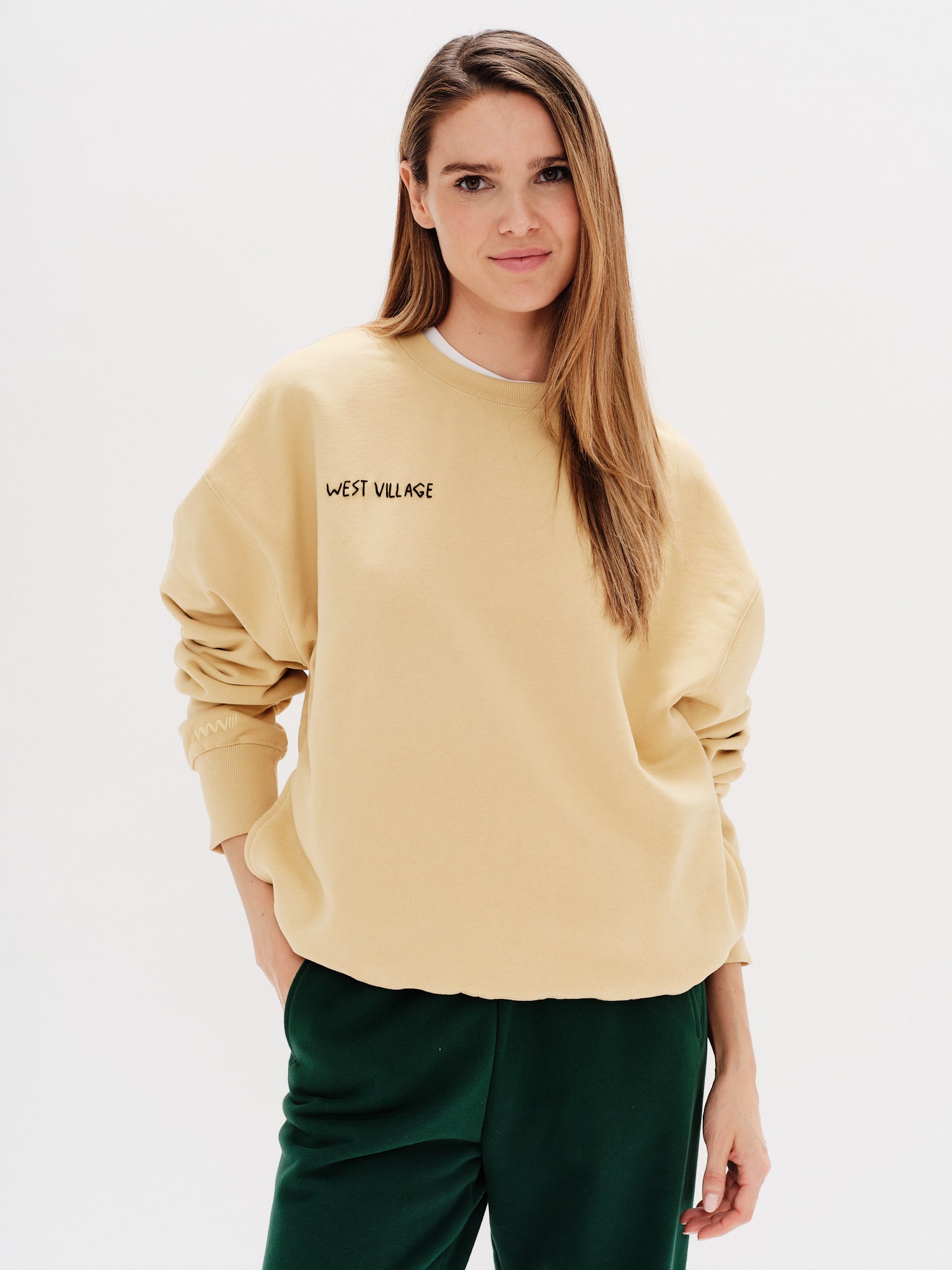 Woman wearing a yellos sweatshirt with embroidered west village text