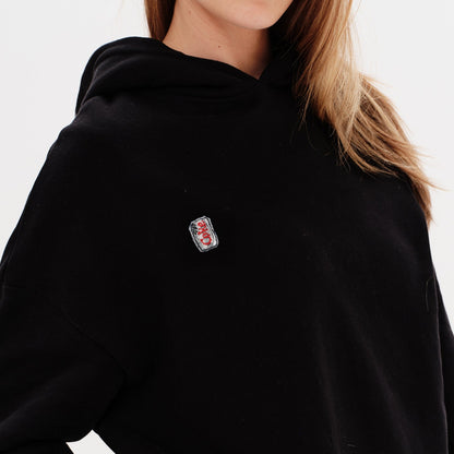 Person wearing a black hoodie with a small diet coke embroidery on a white background