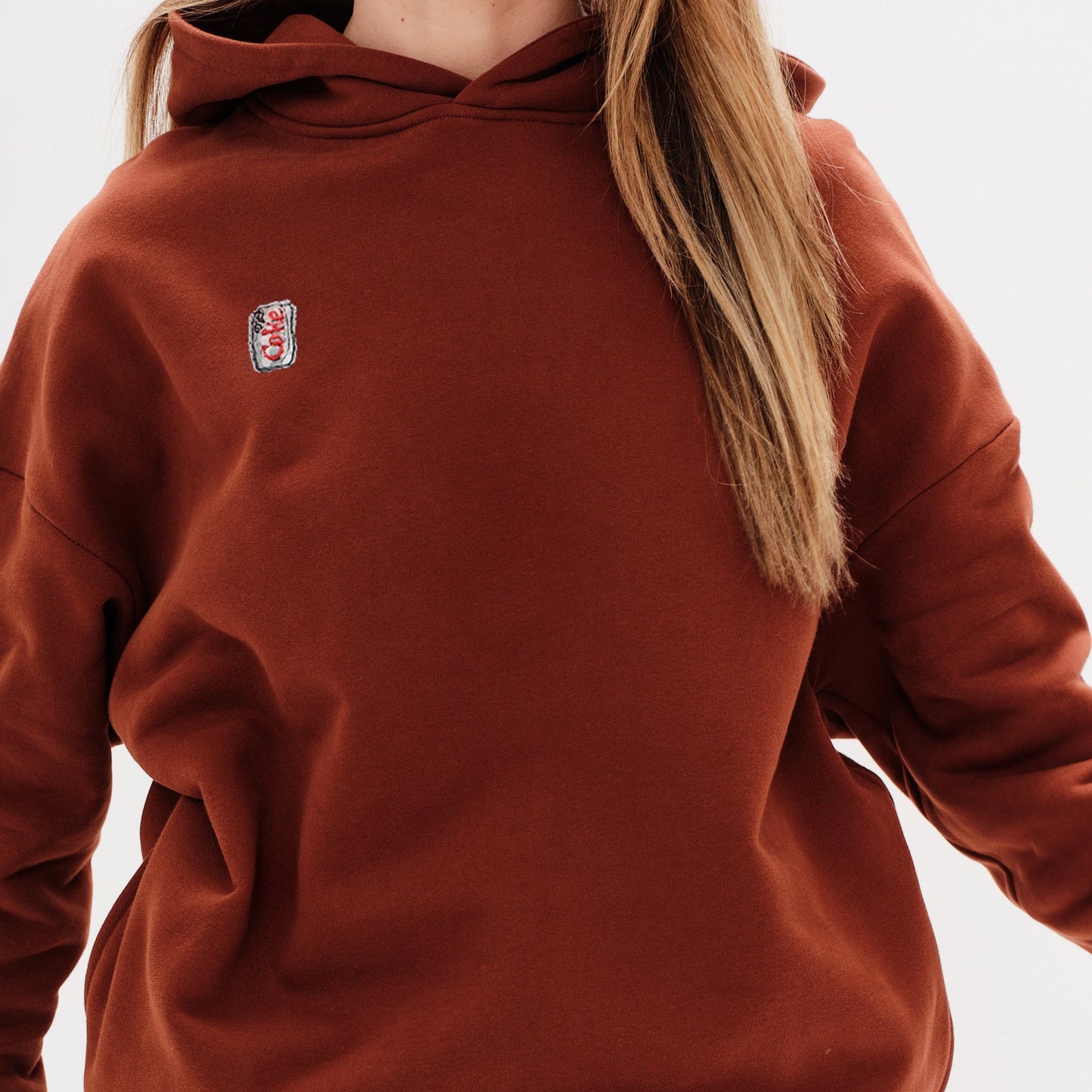 Person wearing a brown hoodie with a small diet coke embroidery on a white background