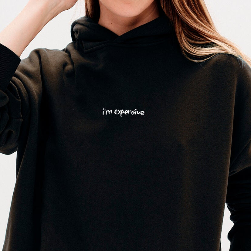 Woman wearing a black hoodie with an I'm expensive embroidered text 