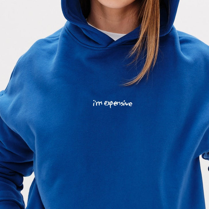 Woman wearing a blue hoodie with an I'm expensive embroidered text 
