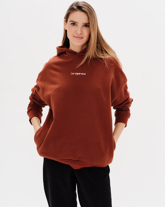 Woman wearing a brown hoodie with an I'm expensive embroidered text 