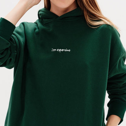 Woman wearing a green hoodie with an I'm expensive embroidered text 