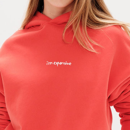 Woman wearing an orange hoodie with an I'm expensive embroidered text 