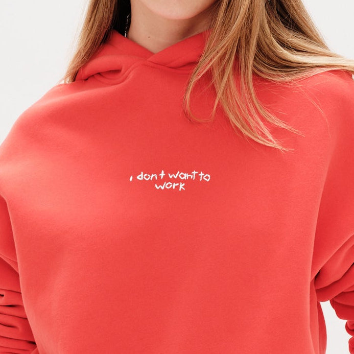 Woman wearing an orange sweatshirt with I don't want to work embroidery text