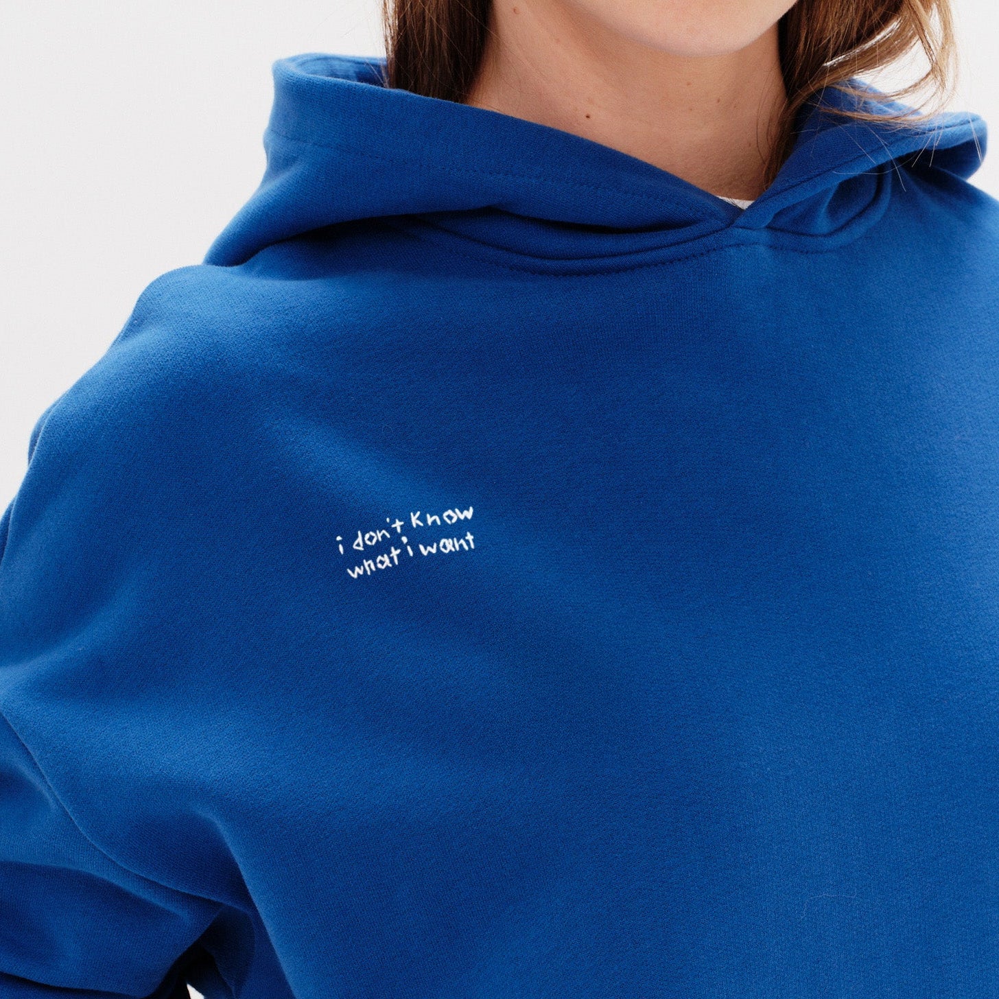 Woman wearing a blue hoodie with an I don't know what I want embroidery text