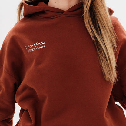 Woman wearing a brown hoodie with an I don't know what I want embroidery text