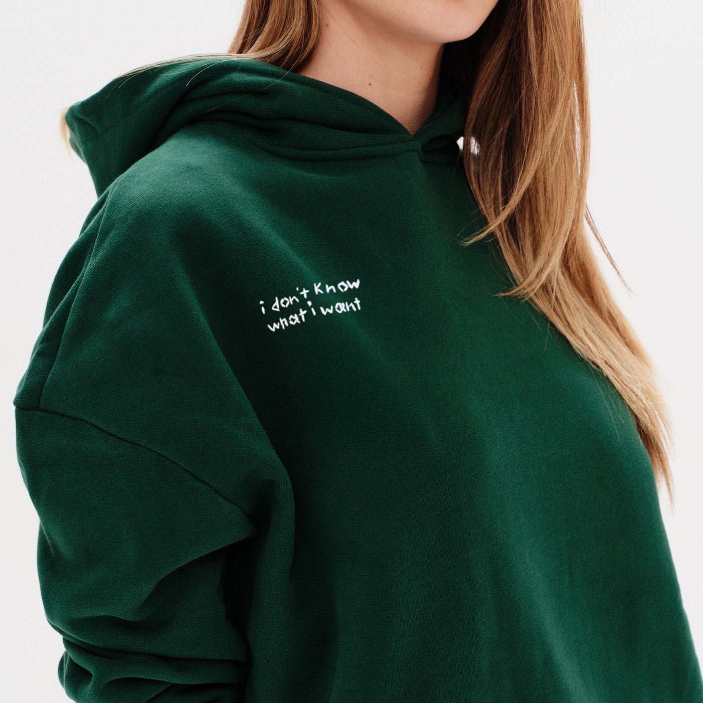 Woman wearing a green hoodie with an I don't know what I want embroidery text
