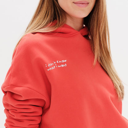 Woman wearing an orange hoodie with an I don't know what I want embroidery text
