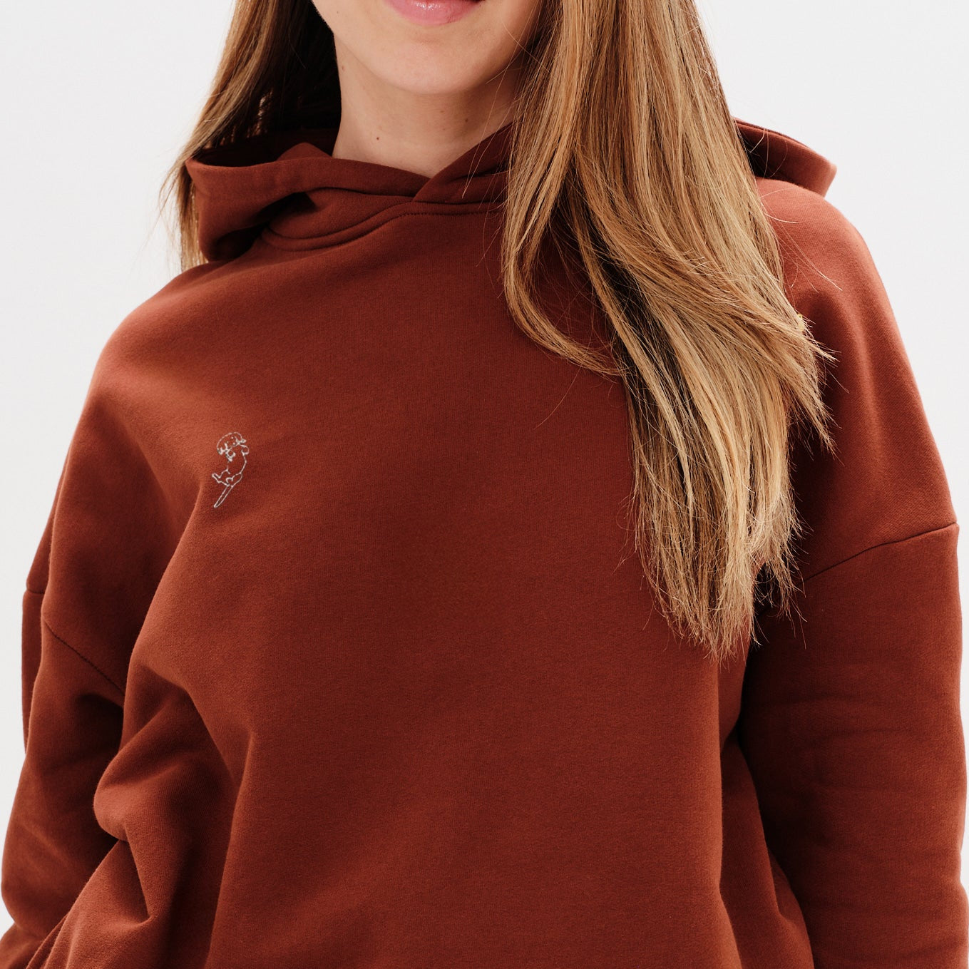 Person wearing a brown hoodie with a small wiener dog embroidery on a white background