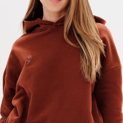 Person wearing a brown hoodie with a small wiener dog embroidery on a white background