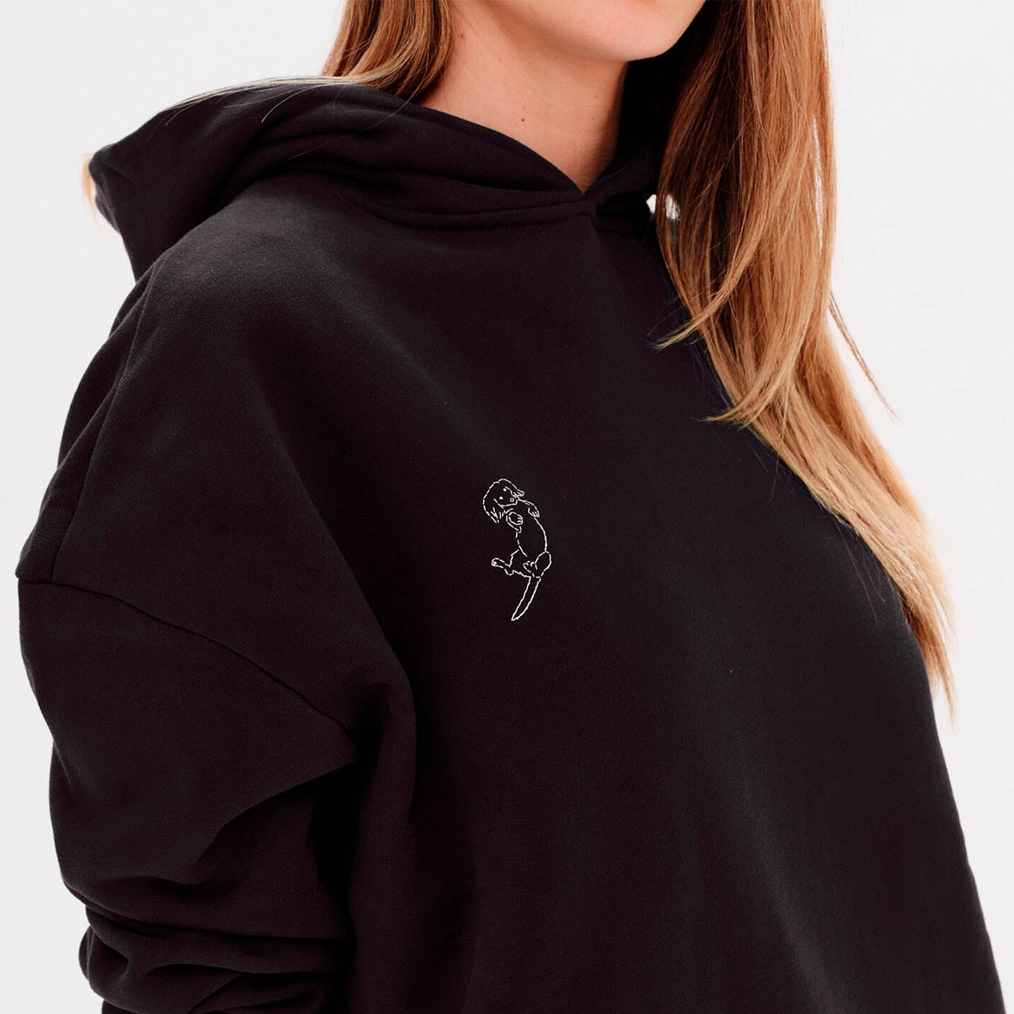 Person wearing a black hoodie with a small white  on wiener dog embroidery in a plain background