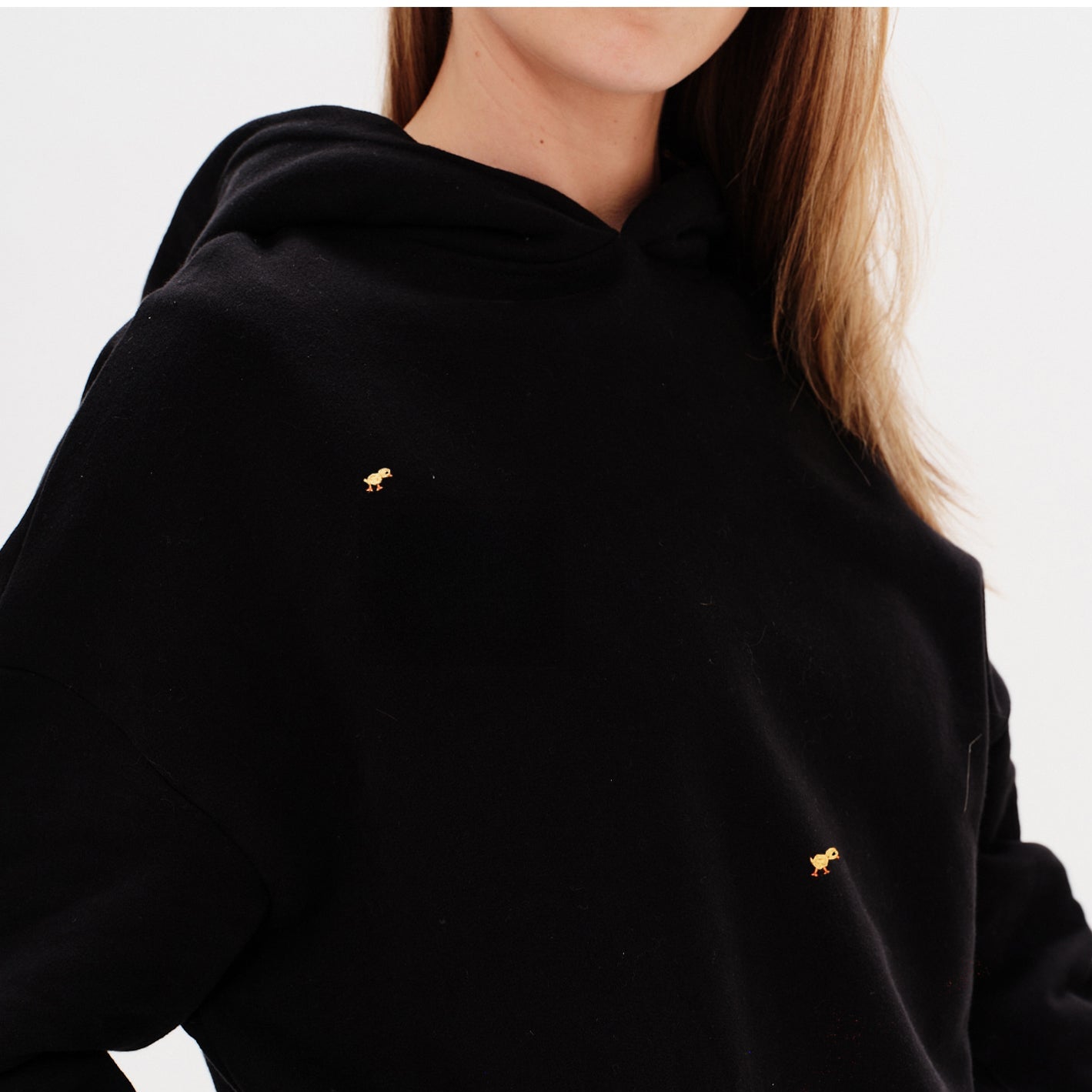 Woman wearing a black premium hoodie with a mini duck embroidery