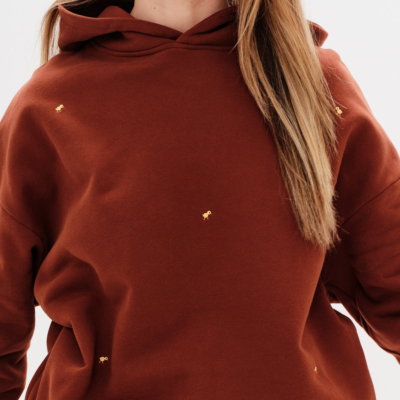 Woman wearing a brown premium hoodie with a mini duck embroidery