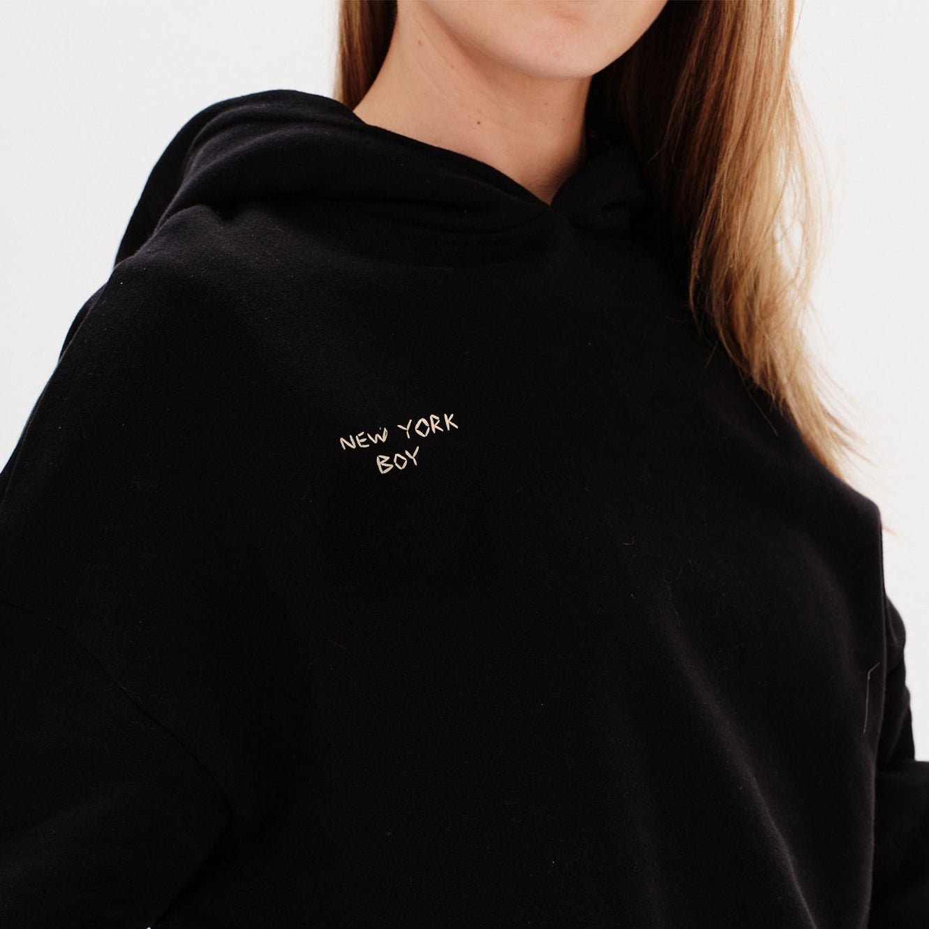 Woman wearing a black hoodie with a New York Boy embroidery text