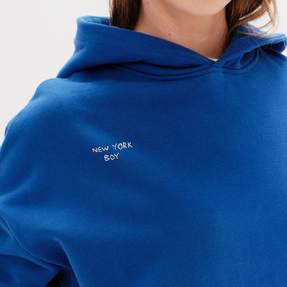 Woman wearing a blue hoodie with a New York Boy embroidery text