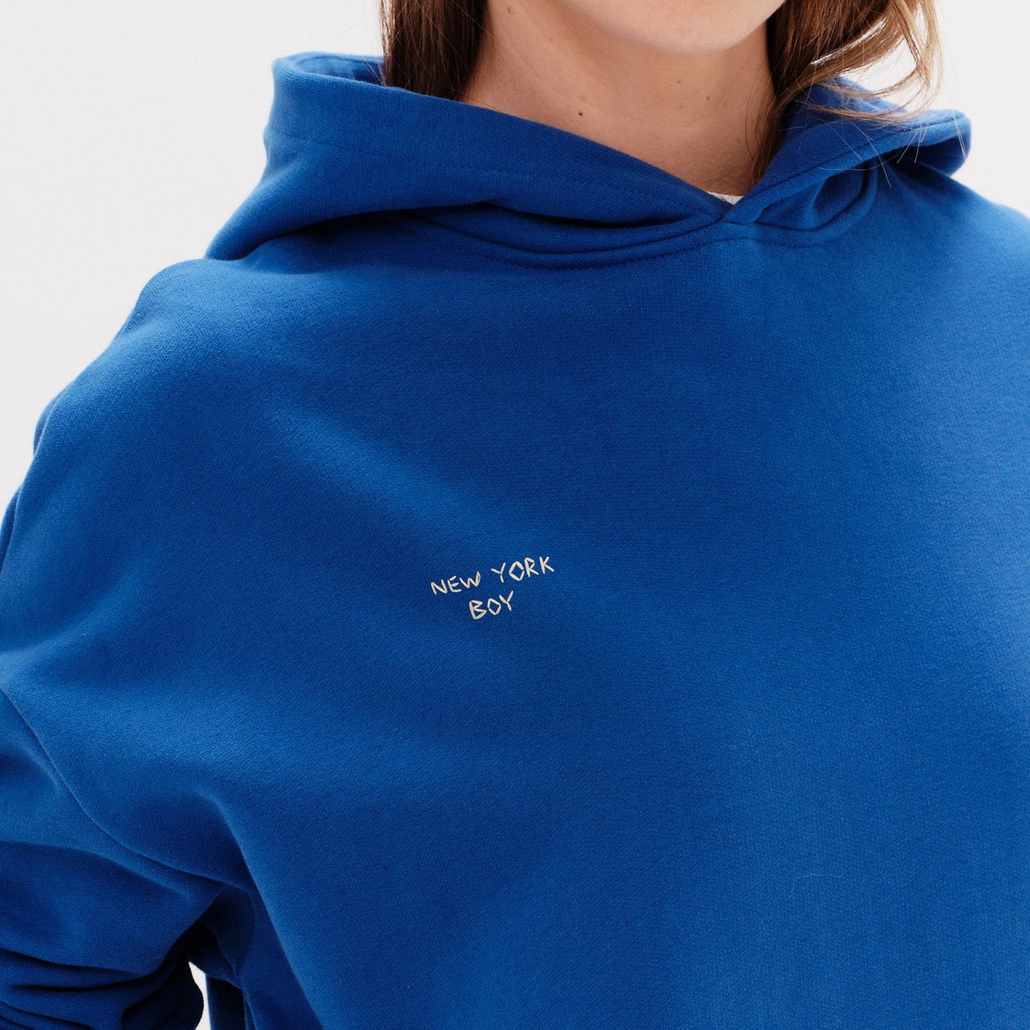 Woman wearing a blue hoodie with a New York Boy embroidery text