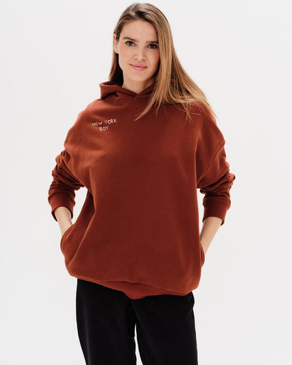 Woman wearing a brown hoodie with a New York Boy embroidery text
