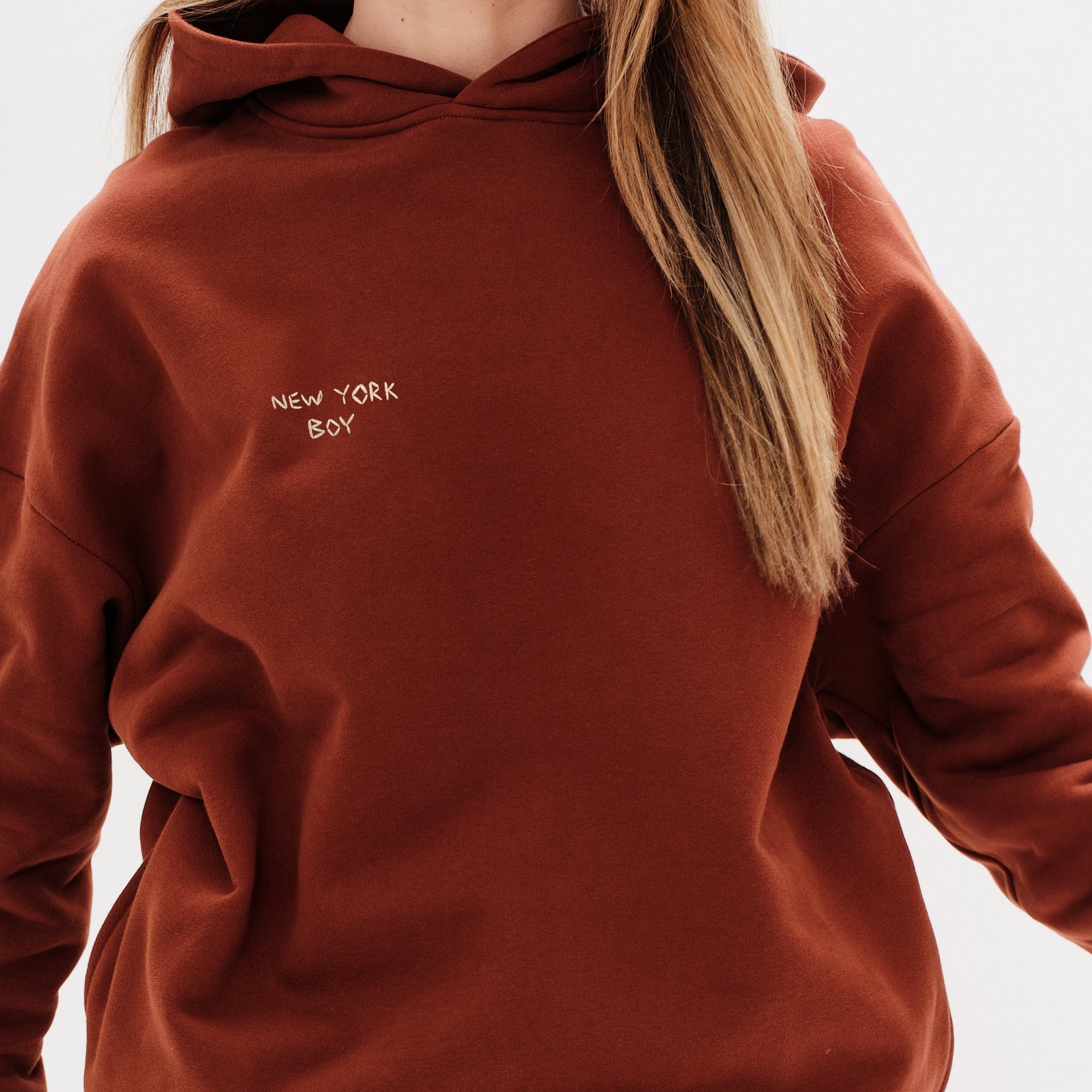 Woman wearing a brown hoodie with a New York Boy embroidery text