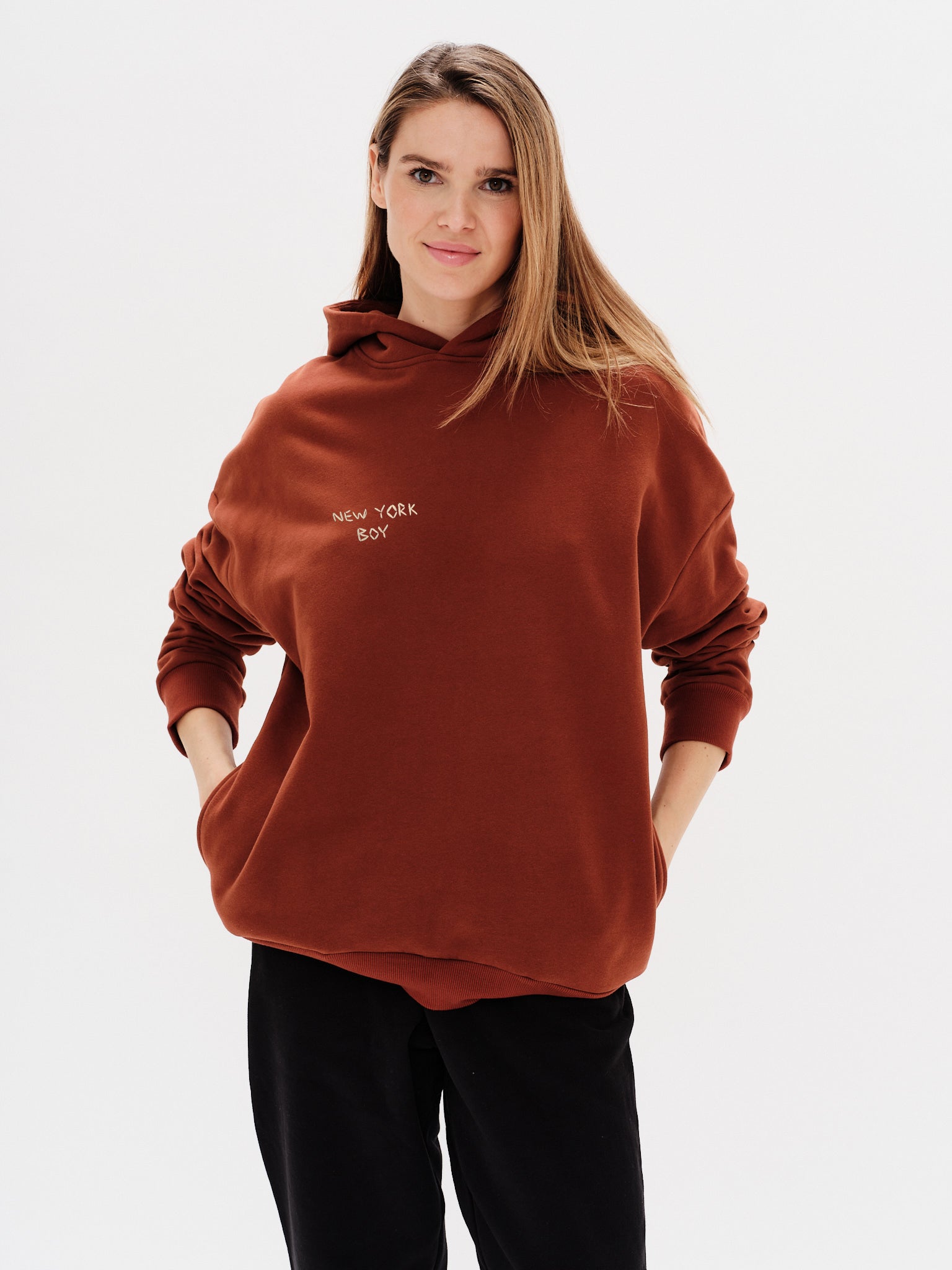 Woman wearing a brown hoodie with a New York Boy embroidery text